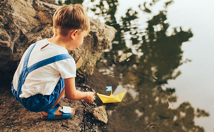 boy with paper boat near water